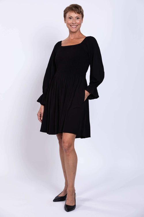 Woman wearing a black dress with shirred bodice, square neckline, and ruffled sleeves