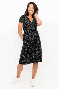Woman smiling in a black polka dot dress with V-neckline and pockets, angled front view