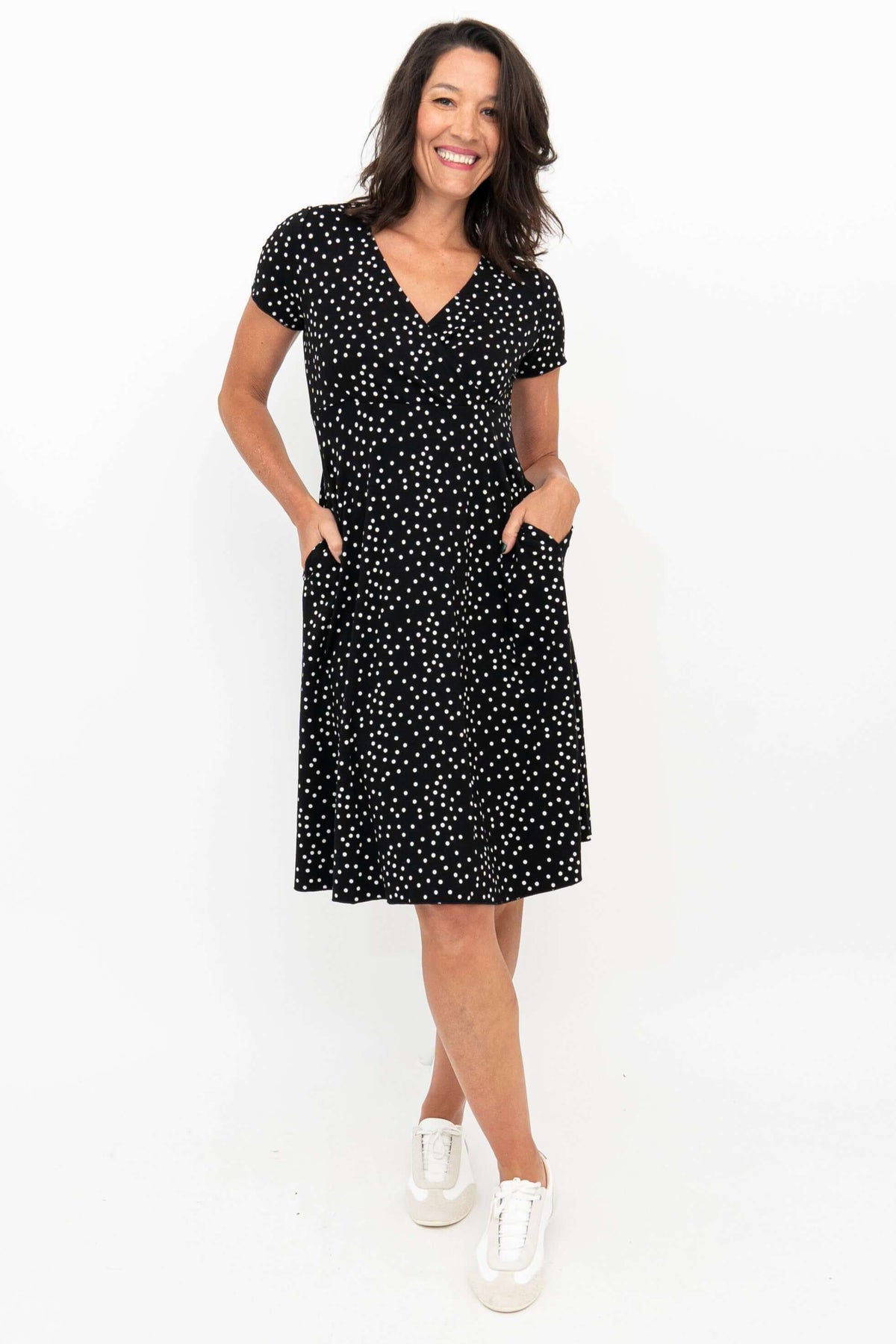 Woman wearing a black polka dot short sleeve dress with pockets, front view