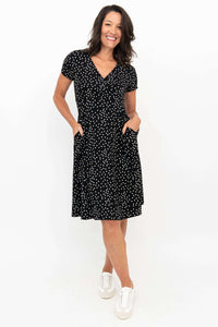 Woman wearing a black polka dot short sleeve dress with pockets, front view