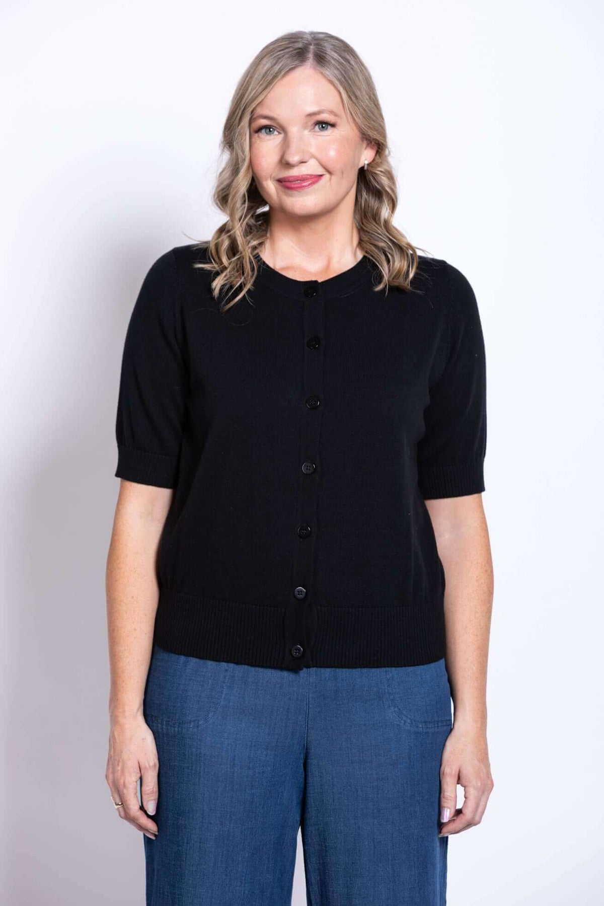Woman wearing a black short-sleeve button-up cotton cardigan with blue pants