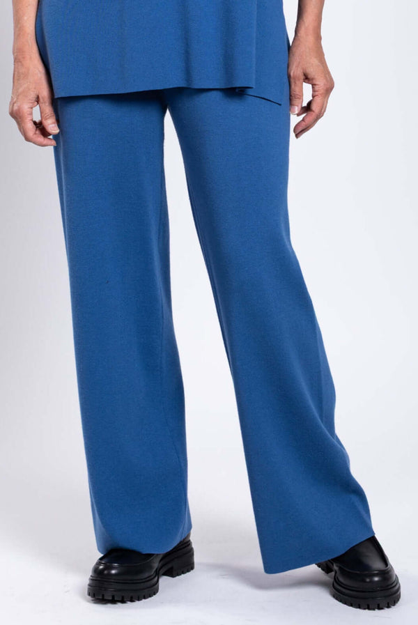 Close-up of woman's legs wearing blue knit pants and black shoes against a white background