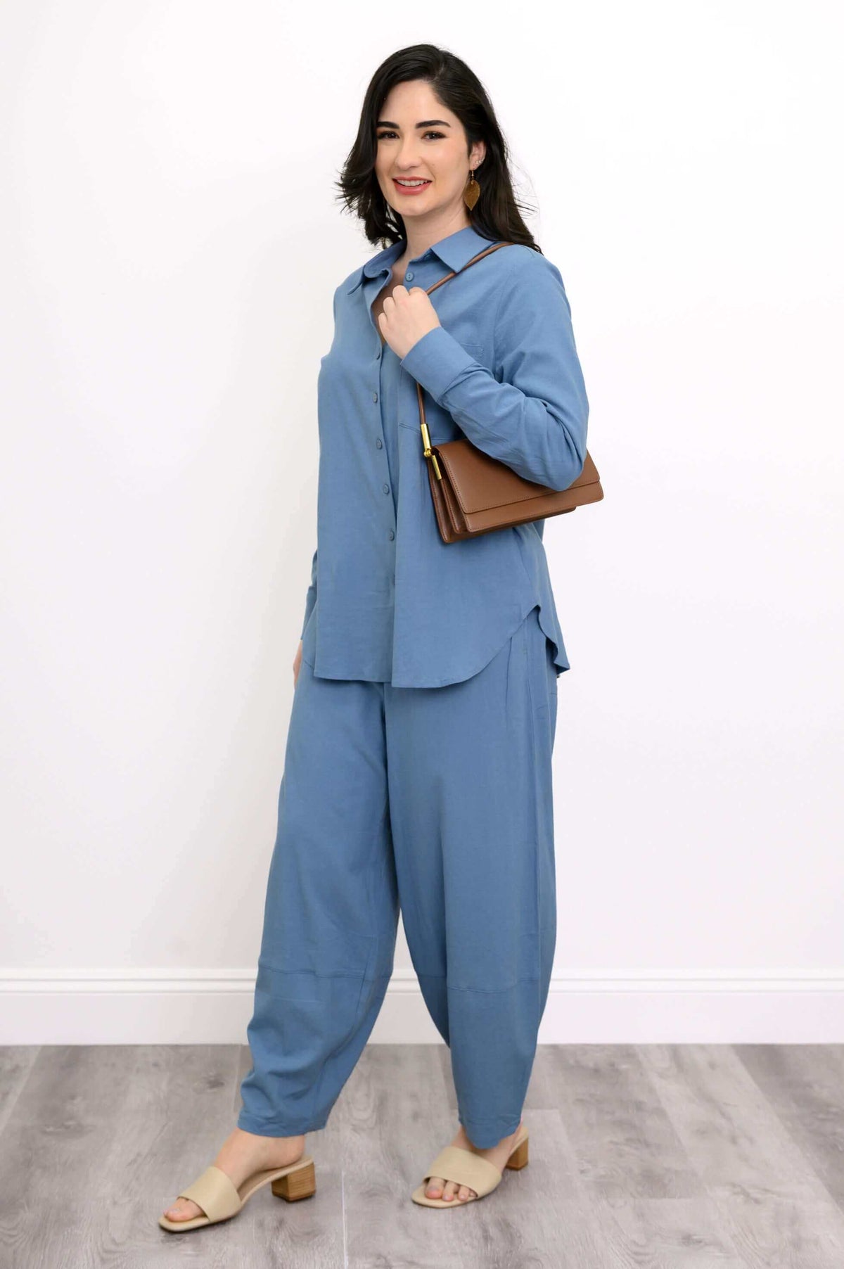Woman in blue set with a brown shoulder bag on her arm, standing against a white wall