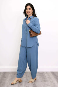Woman in blue set with a brown shoulder bag on her arm, standing against a white wall
