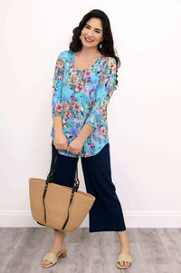Woman posing in blue floral top with navy pants and tan bag