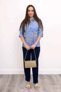 Model standing in a blue floral blouse, navy pants, beige purse and sandals