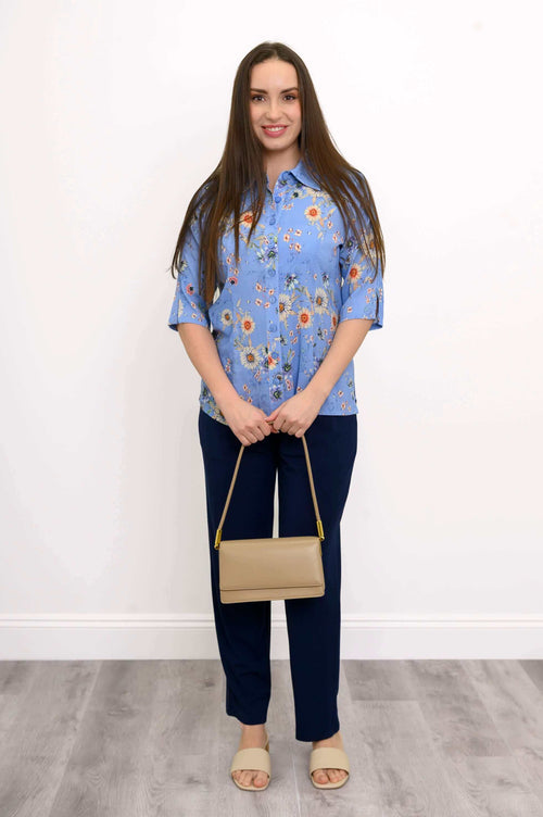 Model standing in a blue floral blouse, navy pants, beige purse and sandals