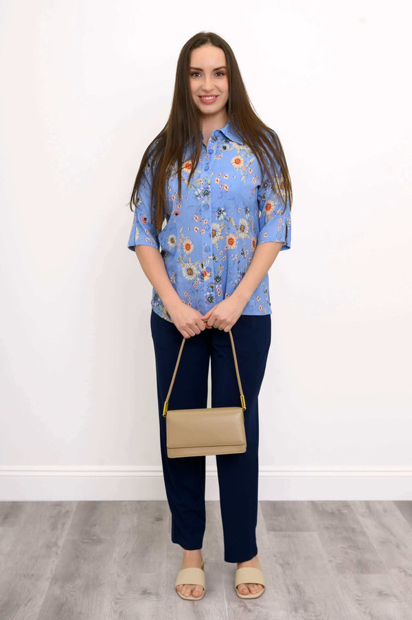 Model standing in a blue floral blouse, navy pants, beige purse and sandals
