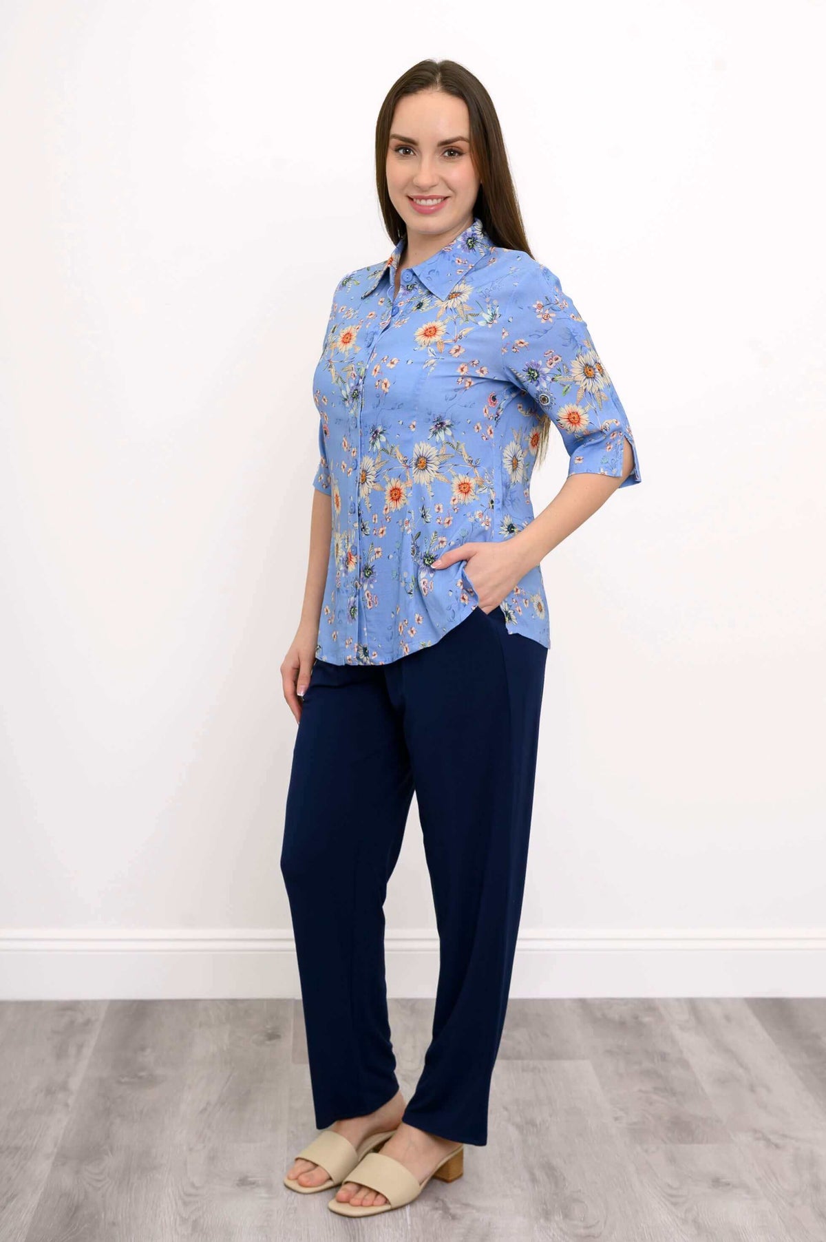 Model in blue floral blouse and navy pants with hand in pocket, angled pose