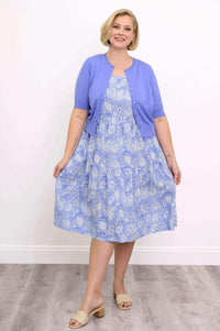 Woman in a blue floral dress and lilac cardigan holding her skirt with both hands