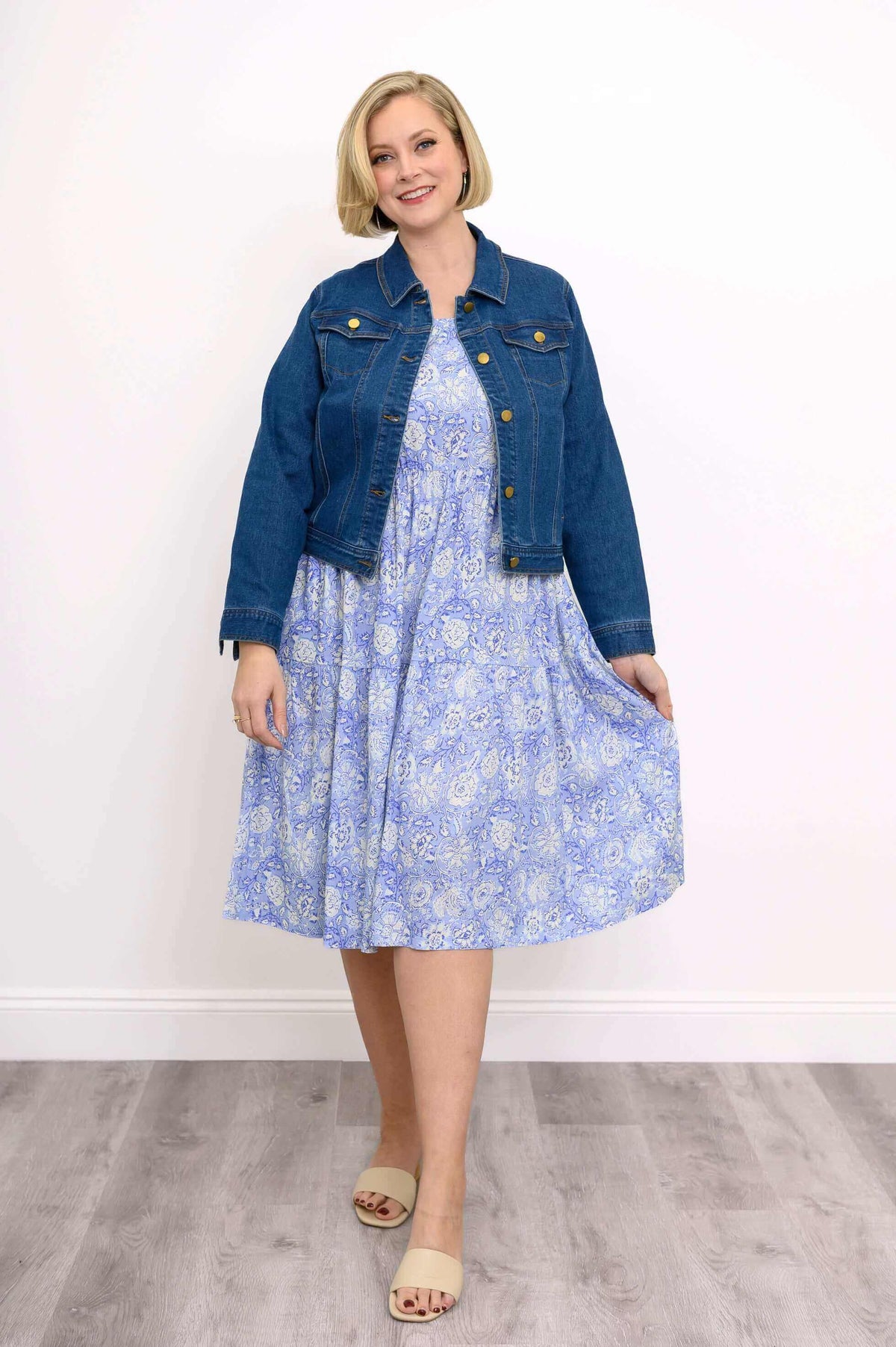 Woman wearing a blue floral dress styled with a denim jacket and beige sandals