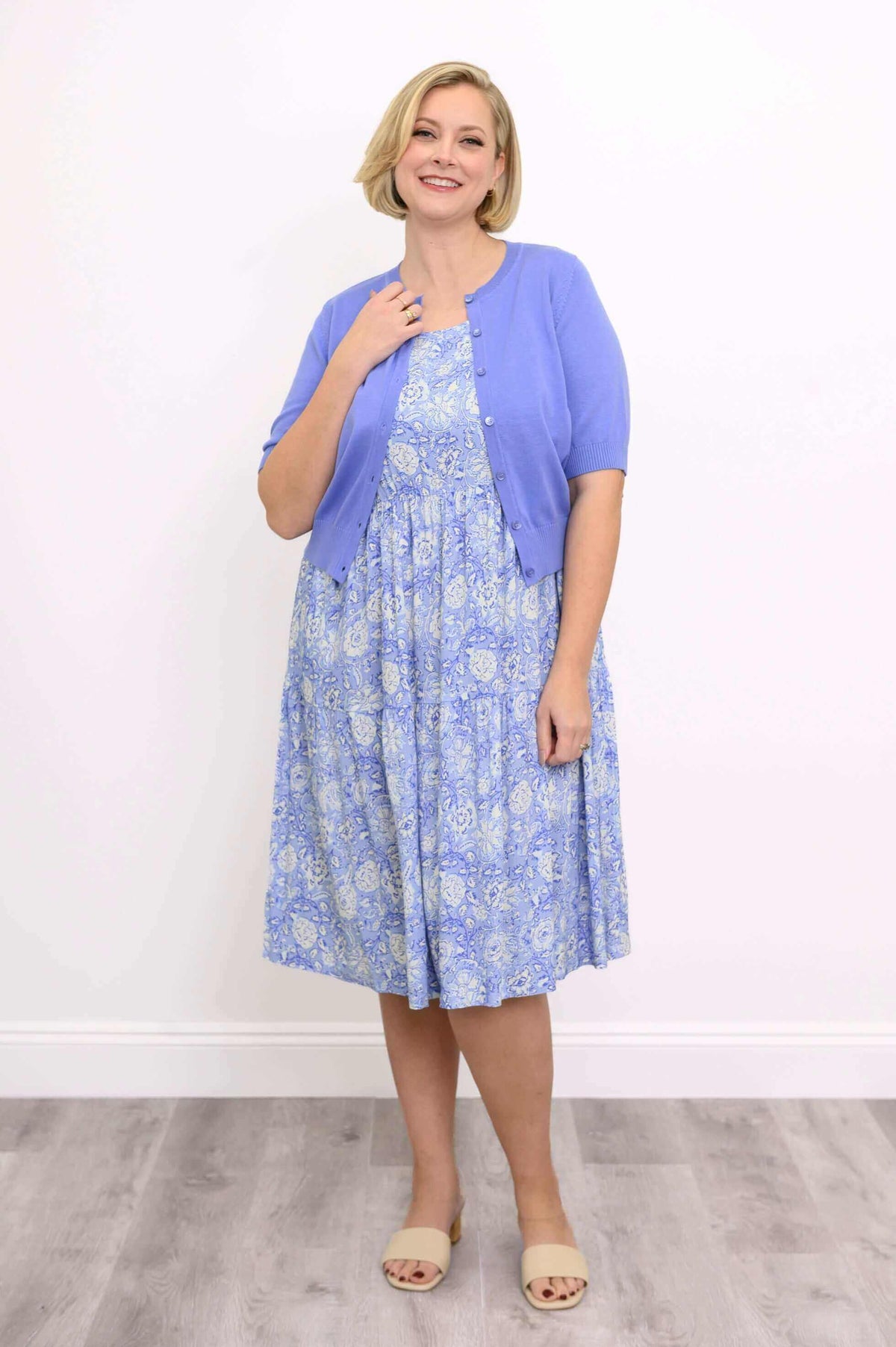 Woman smiling in a blue floral dress paired with a blue cardigan and beige sandals