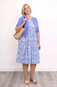 Woman carrying a straw tote bag in a blue floral dress and lilac cardigan