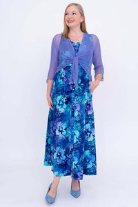 Woman in a blue floral maxi dress and purple cardigan, standing upright and smiling