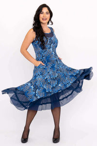 Woman posing with hands in pockets, blue floral mesh-trimmed dress swirling