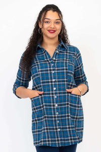 Woman wearing a blue plaid button-up flannel tunic with hands in pockets