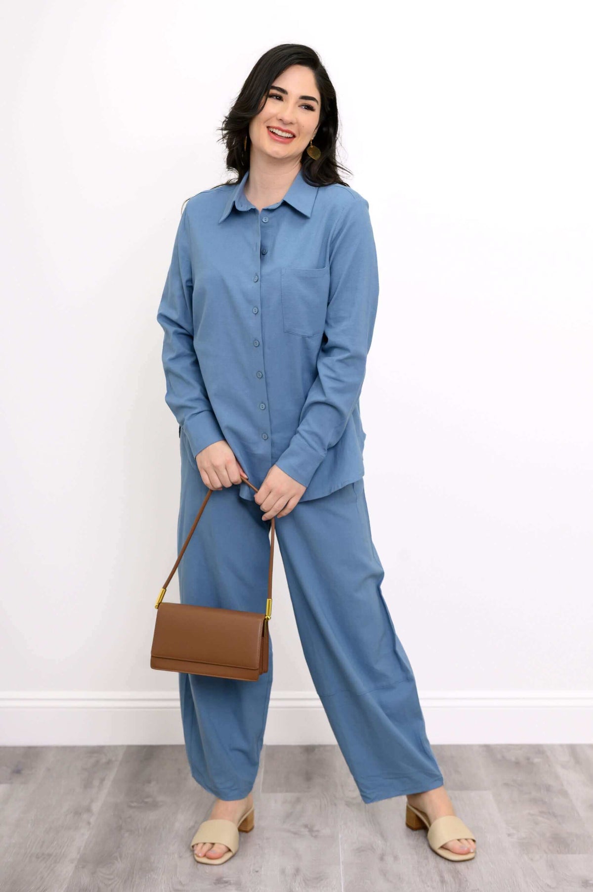 Smiling woman in blue shirt and pants holding a brown shoulder bag