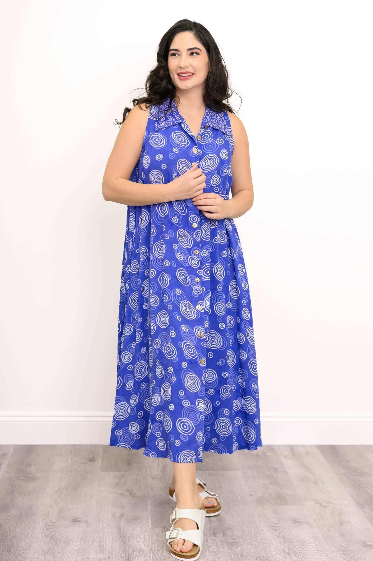Model in blue sleeveless A-line dress with swirl patterns, hands adjusting buttons