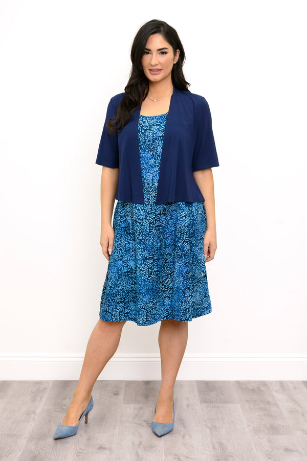 A woman models a two-piece outfit consisting of a navy blue short-sleeve cardigan and a blue patterned dress with a matching blue blazer, set against a plain white wall and light wood flooring.