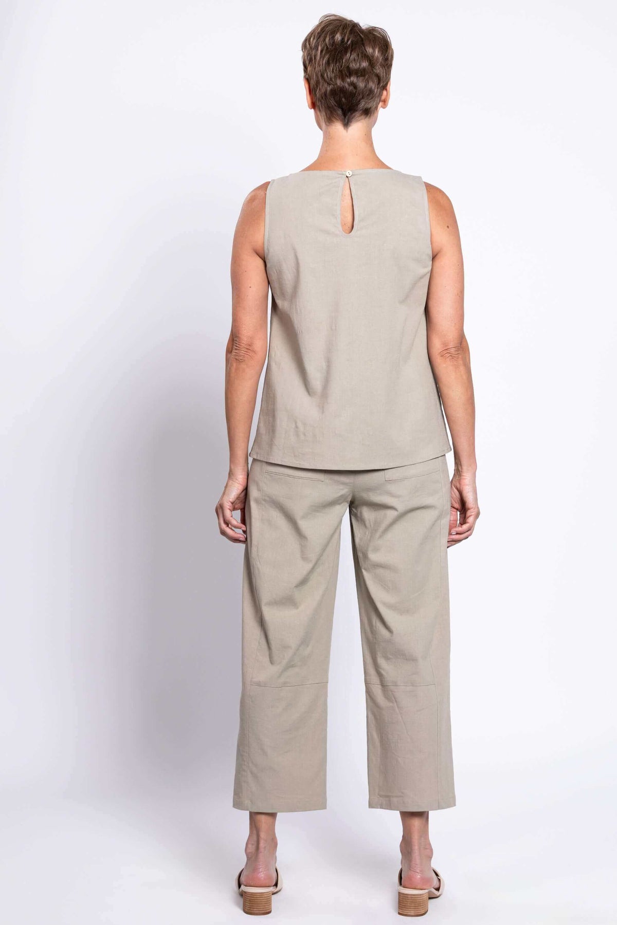 Back view of woman in light beige sleeveless top and cropped barrel-leg pants