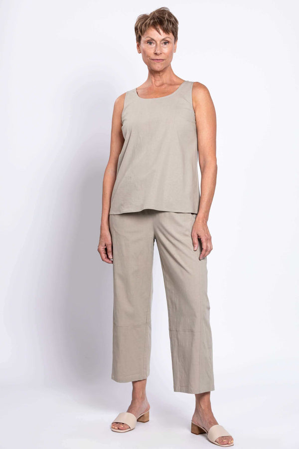 Woman standing in light beige sleeveless top and cropped pants, front view, arms relaxed
