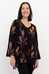 Woman wearing a black bohemian top with colorful leaf print, v-neckline and bell sleeves, smiling
