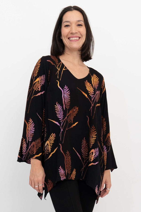 Woman wearing a black bohemian top with colorful leaf print, v-neckline and bell sleeves, smiling