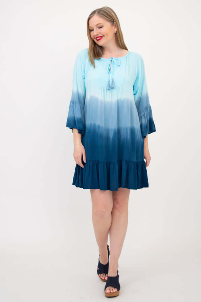 Model posing in the Ellie Dress, blue ombre color with ruffle sleeves and above-knee length