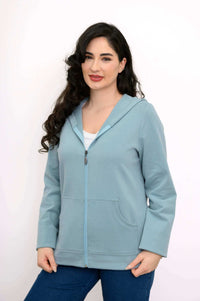Woman standing in a light blue hoodie jacket, smiling and looking forward