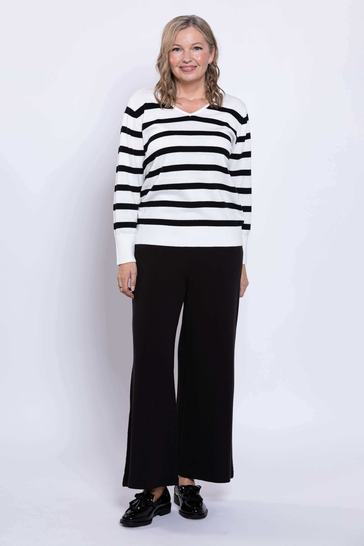 Front view of woman standing in black and white striped V-neck sweater with relaxed fit