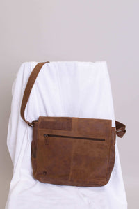 Brown buffalo leather messenger bag displayed on a draped white chair, back zipper visible