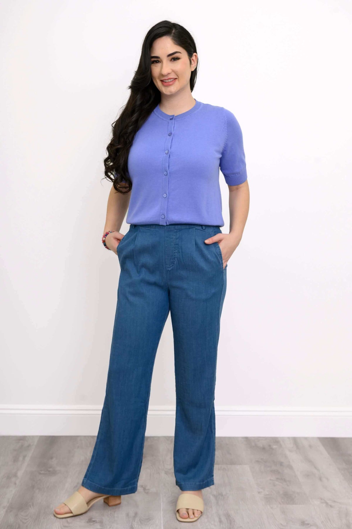 Full body view of a woman in a buttoned purple short sleeve cardigan and blue pants