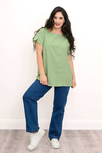 Woman in a sage green straight cut tee, blue jeans, and white sneakers, striking a casual pose