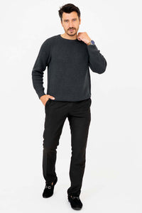 Man modeling a charcoal ribbed sweater and black pants, hand on neck