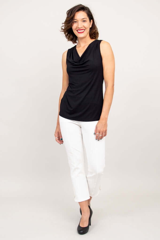 Woman posing in a black sleeveless cowl neck top and white cropped pants