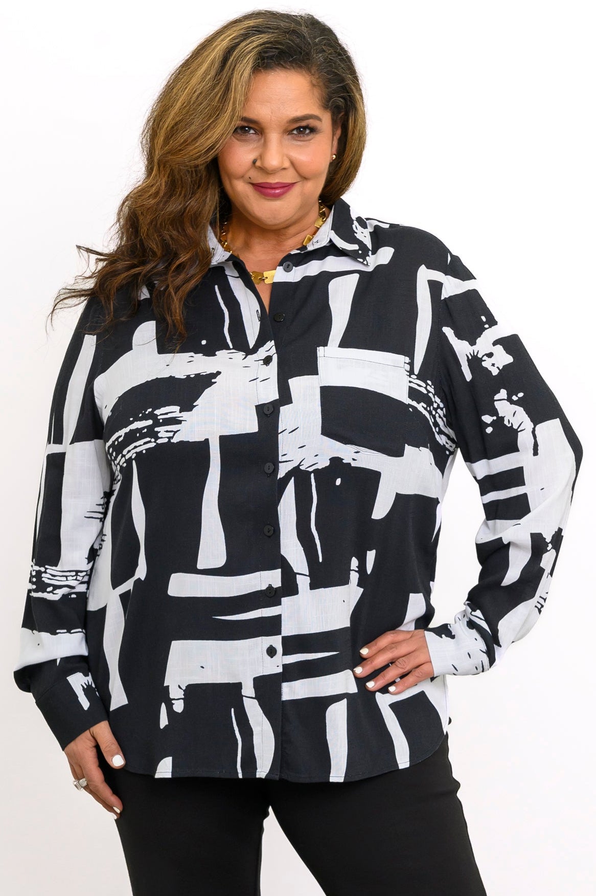 Front view of a smiling woman wearing a long-sleeve button-down blouse in a bold black and white geometric print