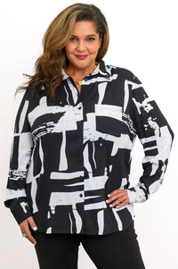 Front view of a smiling woman wearing a long-sleeve button-down blouse in a bold black and white geometric print