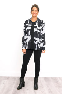 Full-length front view of a smiling woman wearing an open black and white geometric print button-down shirt layered over a black top.