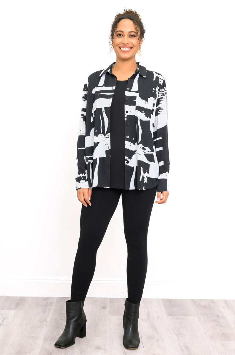 Front view of a female model wearing an unbuttoned black and white long-sleeve blouse with black pants and black boots against a white background and grey floor