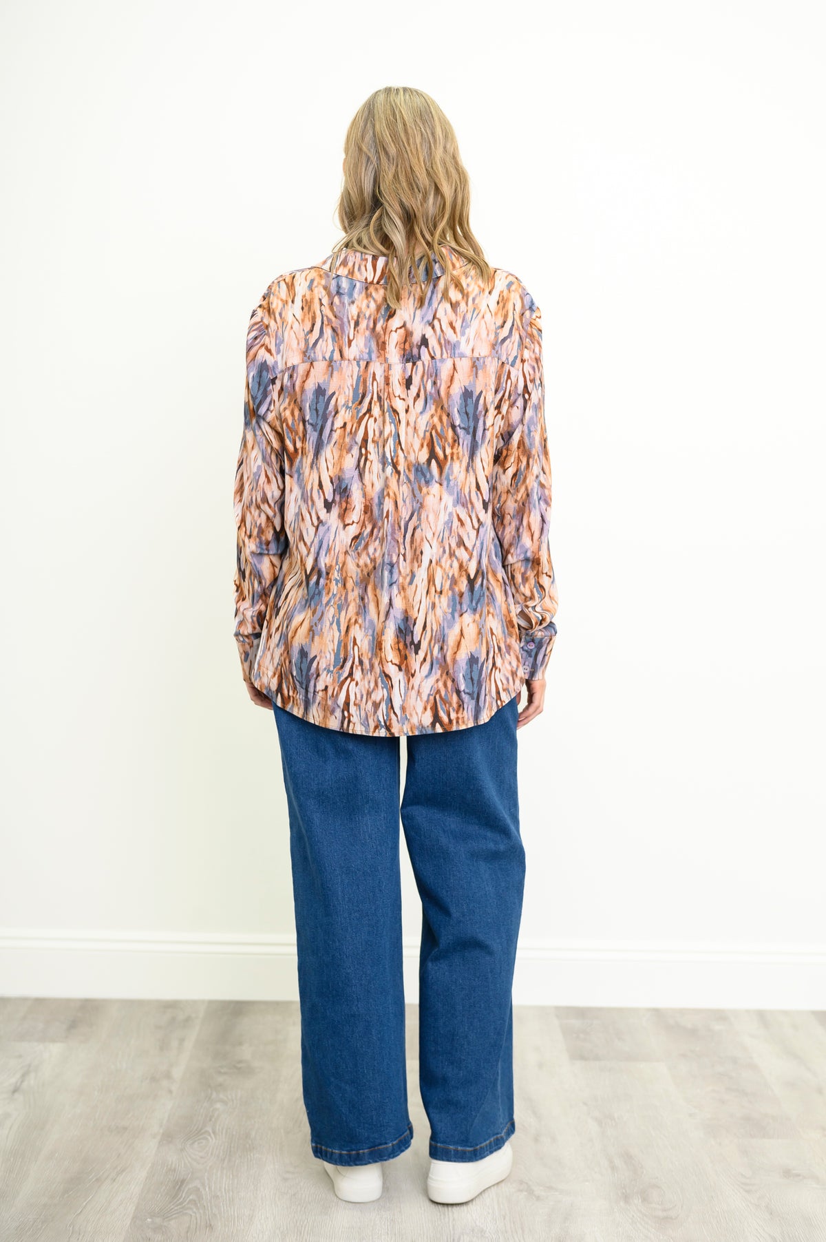 Back view of a woman wearing a relaxed-fit long-sleeve blouse in an abstract earth-tone print with blue jeans