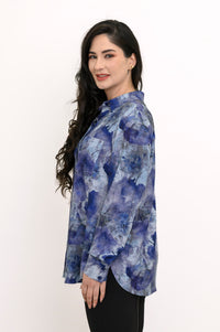 Side view of a smiling woman in a blue watercolor print button-down shirt with a shirt-tail hem.