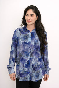 Front view of a woman wearing a blue watercolor print button-down shirt with a spread collar and a breast pocket.
