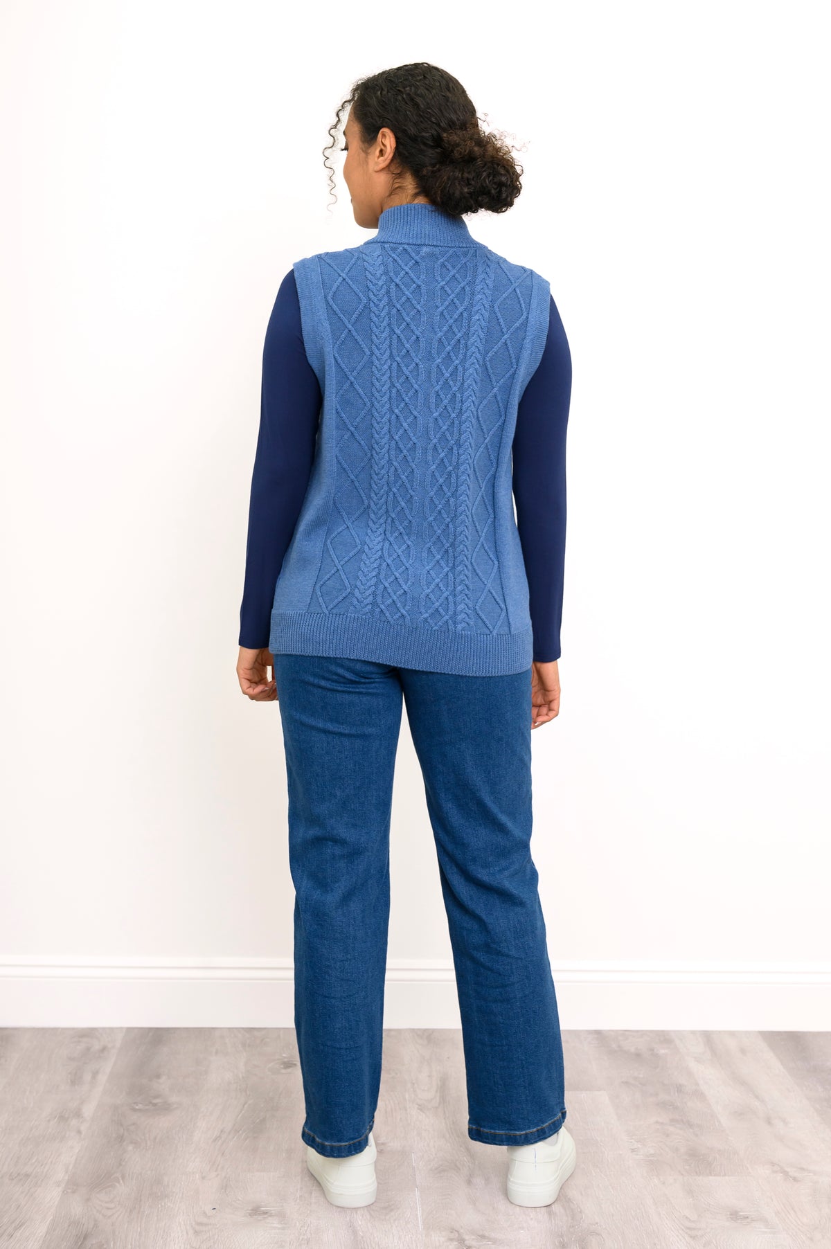 Back view of a blue cable knit vest, highlighting the vertical sweater texture and straight, ribbed hemline.