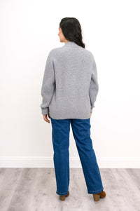 Back view of woman wearing pale grey chunky knit sweater with denim pants and brown heeled boots