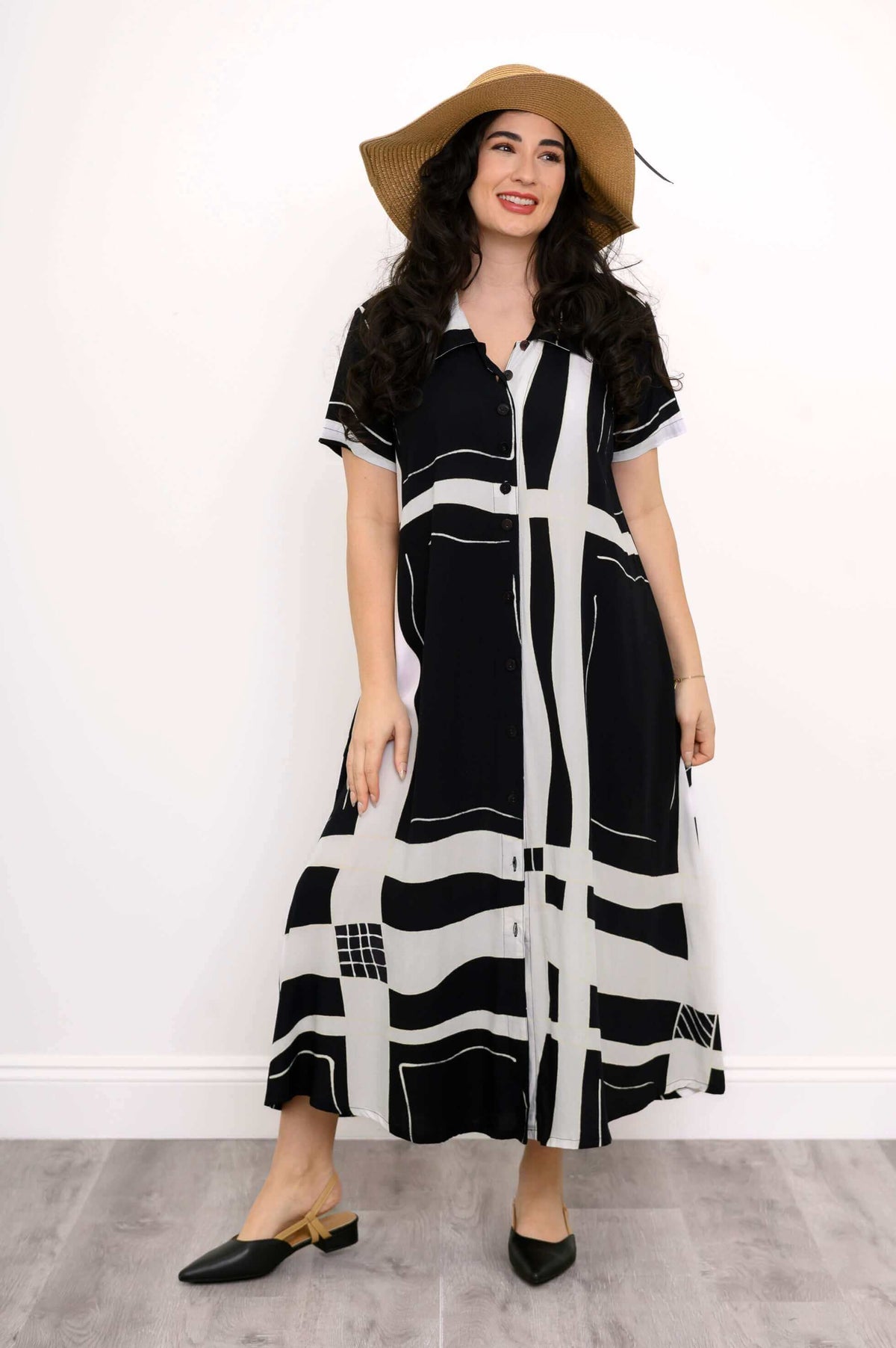 Woman smiling in black and white geometric dress with short sleeves and floppy hat