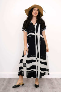 Woman smiling in black and white geometric dress with short sleeves and floppy hat