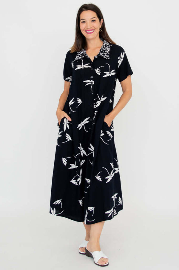Woman wearing a black short sleeve A-line dress with white floral prints, standing with hands in pockets
