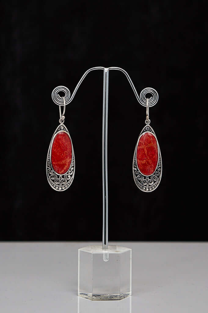 A pair of classic 925 sterling silver drop earrings with vibrant red stones on a display stand