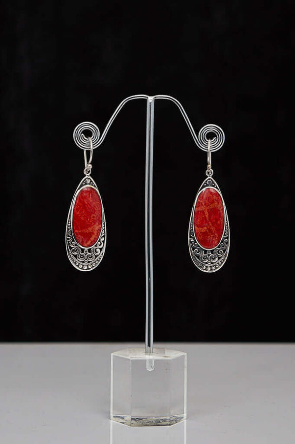 A pair of classic 925 sterling silver drop earrings with vibrant red stones on a display stand