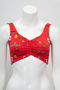 A red ruched bikini top with a playful multicolor print of Canadian flags, birds, and outdoor icons